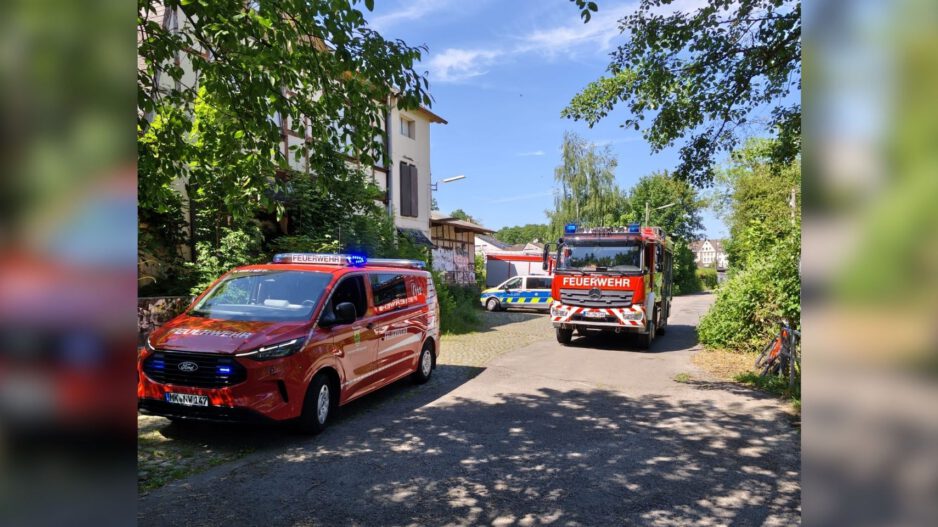 Mehrere Einsatzfahrzeuge von Feuerwehr und Polizei stehen an einer schmalen Straße zwischen Bäumen und Wohnhäusern.
