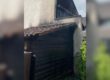An einem Wohnhaus sind deutliche Rußspuren an einer angebauten Holzhütte und am Dachbereich nach einem Brand zu sehen.