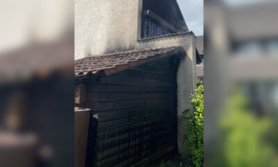 An einem Wohnhaus sind deutliche Rußspuren an einer angebauten Holzhütte und am Dachbereich nach einem Brand zu sehen.