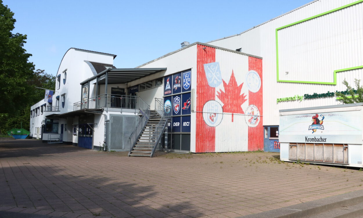 Außenansicht einer Eissporthalle mit Logos der Iserlohn Roosters und großem Ahornblatt an der Fassade.