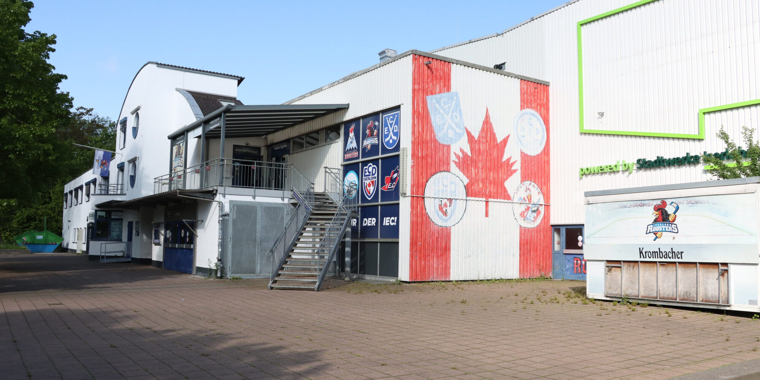 Außenansicht einer Eissporthalle mit Logos der Iserlohn Roosters und großem Ahornblatt an der Fassade.