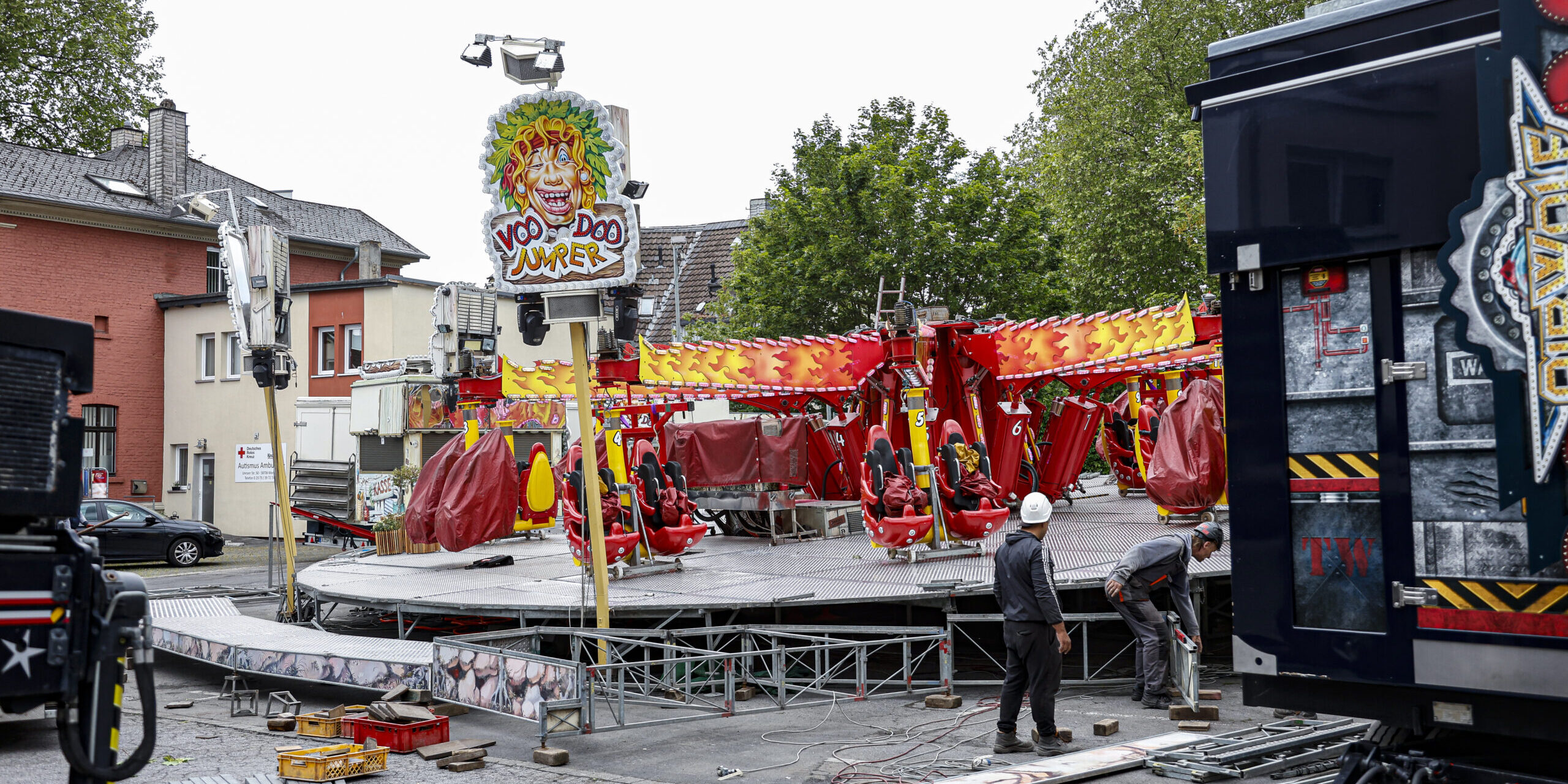 Aufbau eines Fahrgeschäfts auf einem Kirmesplatz: Arbeiter montieren das Karussell „VooDoo Jumper“ zwischen verstreuten Bauteilen und Fahrzeugen.