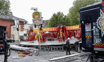 Aufbau eines Fahrgeschäfts auf einem Kirmesplatz: Arbeiter montieren das Karussell „VooDoo Jumper“ zwischen verstreuten Bauteilen und Fahrzeugen.
