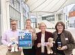 Vier Personen präsentieren ein Plakat und Werbeartikel zum 300-jährigen Jubiläum der Mendener Pfingstkirmes in einem überdachten Innenhof.
