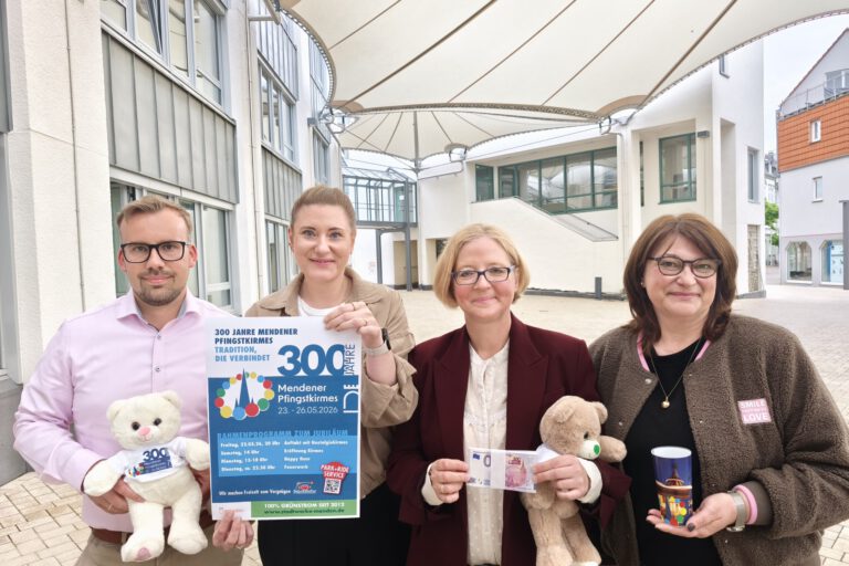 Vier Personen präsentieren ein Plakat und Werbeartikel zum 300-jährigen Jubiläum der Mendener Pfingstkirmes in einem überdachten Innenhof.