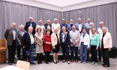 Gruppenfoto einer Ehrungsveranstaltung mit mehr als 20 Personen in einem Saal. Die Teilnehmenden stehen in mehreren Reihen vor einer grauen Vorhangwand. Im Vordergrund befindet sich eine Frau mit Bürgermeisterkette, umgeben von den geehrten Bürgerinnen und Bürgern verschiedener Altersgruppen. Links im Bild ist ein Klavier zu sehen.