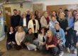 Gruppenfoto von rund 25 Teilnehmenden einer Veranstaltung zur Kindertagespflege in einem Gemeinschaftsraum. Die Gruppe steht und kniet für das Foto, daneben ist ein Banner mit der Aufschrift „Gut betreut in Kindertagespflege“ zu sehen. Im Vordergrund rechts ist ein Kind aus Datenschutzgründen verpixelt.