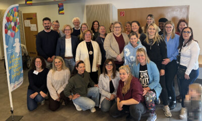 Gruppenfoto von rund 25 Teilnehmenden einer Veranstaltung zur Kindertagespflege in einem Gemeinschaftsraum. Die Gruppe steht und kniet für das Foto, daneben ist ein Banner mit der Aufschrift „Gut betreut in Kindertagespflege“ zu sehen. Im Vordergrund rechts ist ein Kind aus Datenschutzgründen verpixelt.