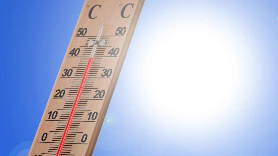 Ein Holzthermometer zeigt an einem sonnigen Tag eine Temperatur von rund 40 Grad Celsius an. Im Hintergrund strahlt eine helle Sonne vor einem wolkenlosen blauen Himmel. Die Aufnahme symbolisiert starke Sommerhitze und hohe Temperaturen.