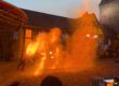Eine Feuershow findet am Abend auf einem historischen Burghof statt. Vor einer Bühne erzeugt ein Künstler mit brennenden Requisiten und Funken spektakuläre Flammenbilder, die den Platz in warmes orangefarbenes Licht tauchen. Zahlreiche Zuschauer verfolgen die Vorführung rund um den Platz, einige halten den Moment mit ihren Smartphones fest.