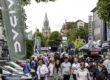 Eine belebte Einkaufsstraße während einer Veranstaltung. Zahlreiche Menschen gehen zwischen Verkaufsständen, Werbefahnen und ausgestellten Fahrzeugen entlang. Im Hintergrund ragt ein Kirchturm über die von Bäumen gesäumte Innenstadt.