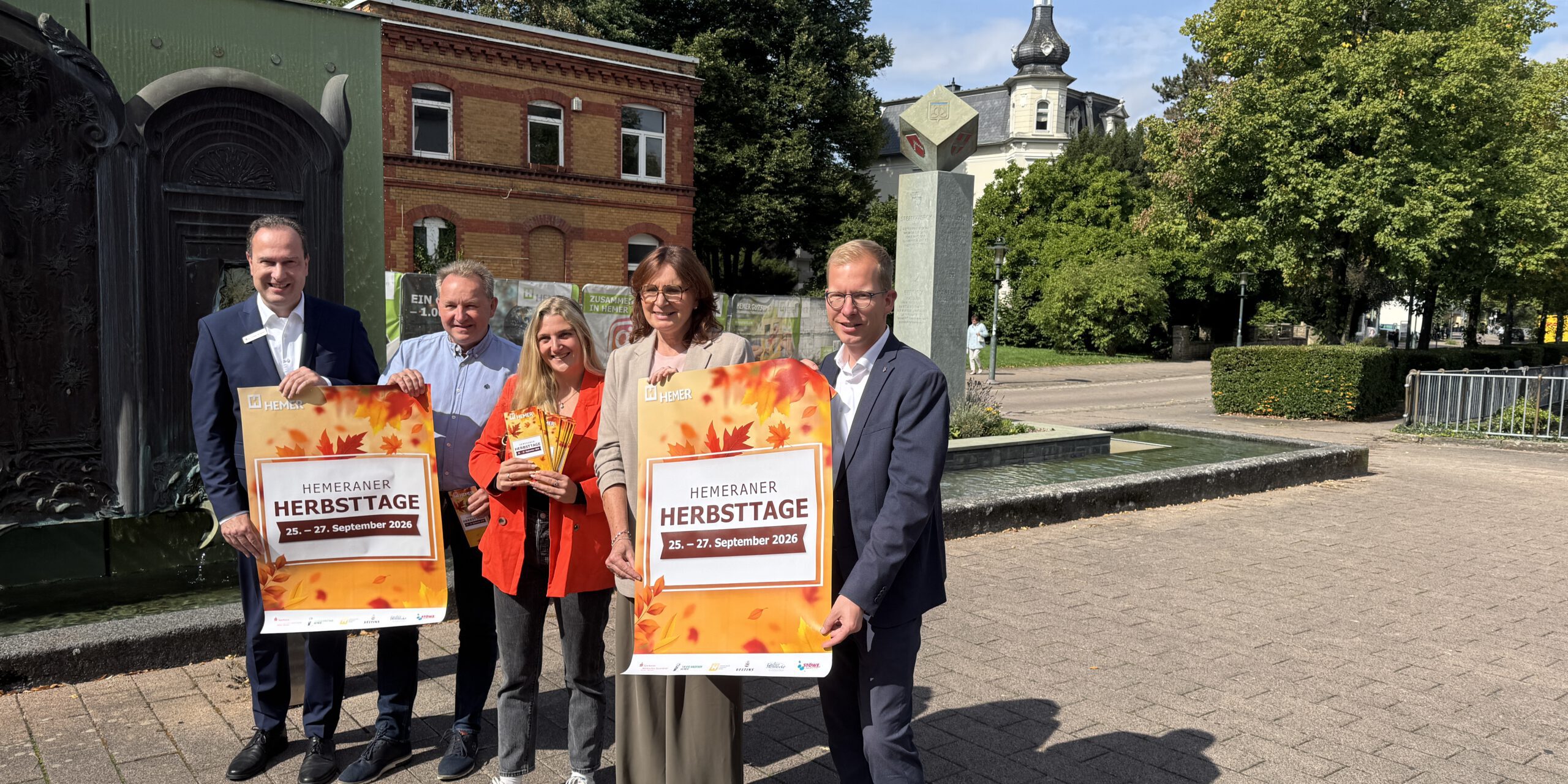 Fünf Personen präsentieren bei sonnigem Wetter vor einer Brunnenanlage in Hemer Plakate für die „Hemeraner Herbsttage“ vom 25. bis 27. September 2026.