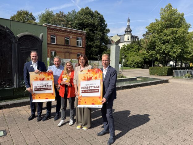 Foto: Giebels/Stadt Hemer Fünf Personen präsentieren bei sonnigem Wetter vor einer Brunnenanlage in Hemer Plakate für die „Hemeraner Herbsttage“ vom 25. bis 27. September 2026.