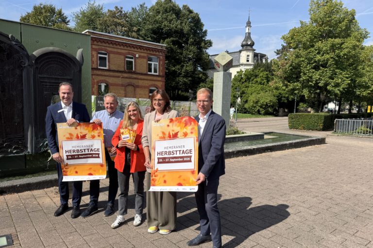 Foto: Giebels/Stadt Hemer Fünf Personen präsentieren bei sonnigem Wetter vor einer Brunnenanlage in Hemer Plakate für die „Hemeraner Herbsttage“ vom 25. bis 27. September 2026.