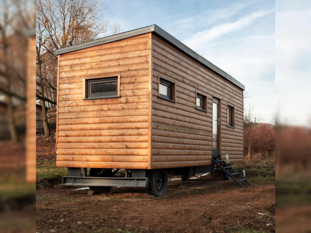 Foto: Milada Vigerova/Pixabay Ein mobiles Tiny House mit Holzfassade steht auf einem Fahrgestell in einer naturnahen Umgebung. Eine kleine Treppe führt zur seitlichen Eingangstür; mehrere Fenster sind in die Holzfassade eingelassen.