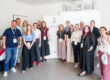 Eine Gruppe von 14 Personen steht für ein gemeinsames Foto in einem hellen Veranstaltungsraum. Die Teilnehmenden tragen Namensschilder an Schlüsselbändern. Im Hintergrund stehen ein Roll-up-Banner der Initiative „5 für Südwestfalen – Smart Cities“ und eine Präsentationsleinwand.